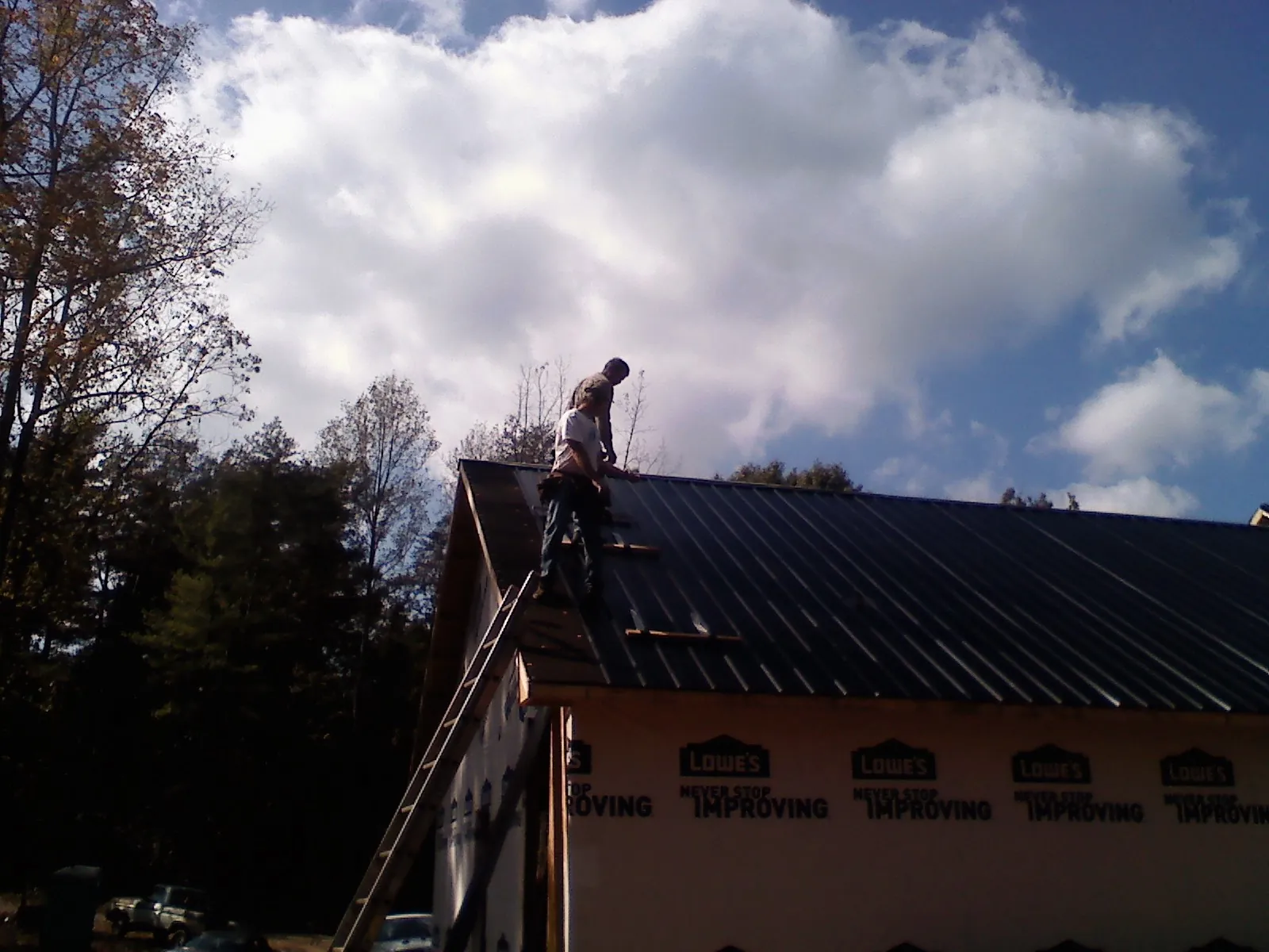 Roofer fastening dark metal panels high against a cloudy sky, from a Roof Inspection job in Taconic