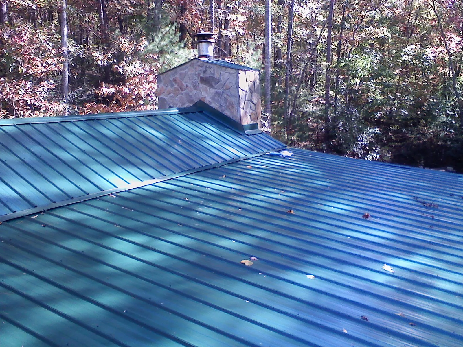 New green metal roof and stone chimney surrounded by autumn woods in Taconic